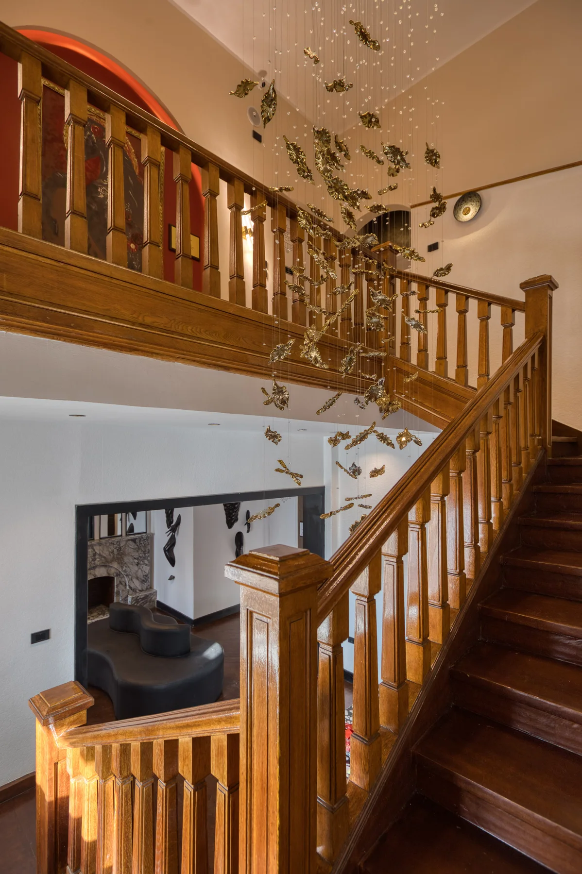 The oak stair climbing under a canopy of gilded brass leaves